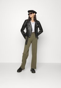 Jaqueta de motoqueiro de couro preta sobre uma t-shirt branca, calças largas verde-oliva, sapatos de plataforma pretos e um boina preta.