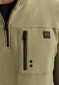 Olijfgroene pullover met een ritszak op de borst, textuurstof en zwarte ritssluiting. Bevat een label met de merknaam "PME Legend".