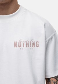Witte katoen t-shirt met korte mouwen, met een beschadigde roze graphic waarop "Good For NOTHING ATELIER" staat op de voorkant.