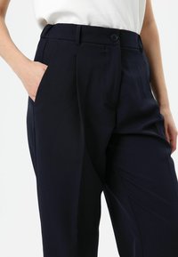 Marineblauwe, op maat gemaakte broek met een gladde textuur, voorzien van een voorzak, knoopsluiting en een recht pijpontwerp.