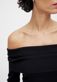 Zwart off-shoulder geribbeld topje met een brede halslijn en een nauwsluitende pasvorm, dat de gestructureerde stof en naadloos ontwerp benadrukt.