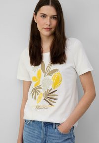 T-shirt en coton blanc avec un imprimé botanique dans des teintes jaunes et vertes, portant la phrase "LA VIE EST UNE COLLECTION DE SOUVENIRS" en écriture cursive.