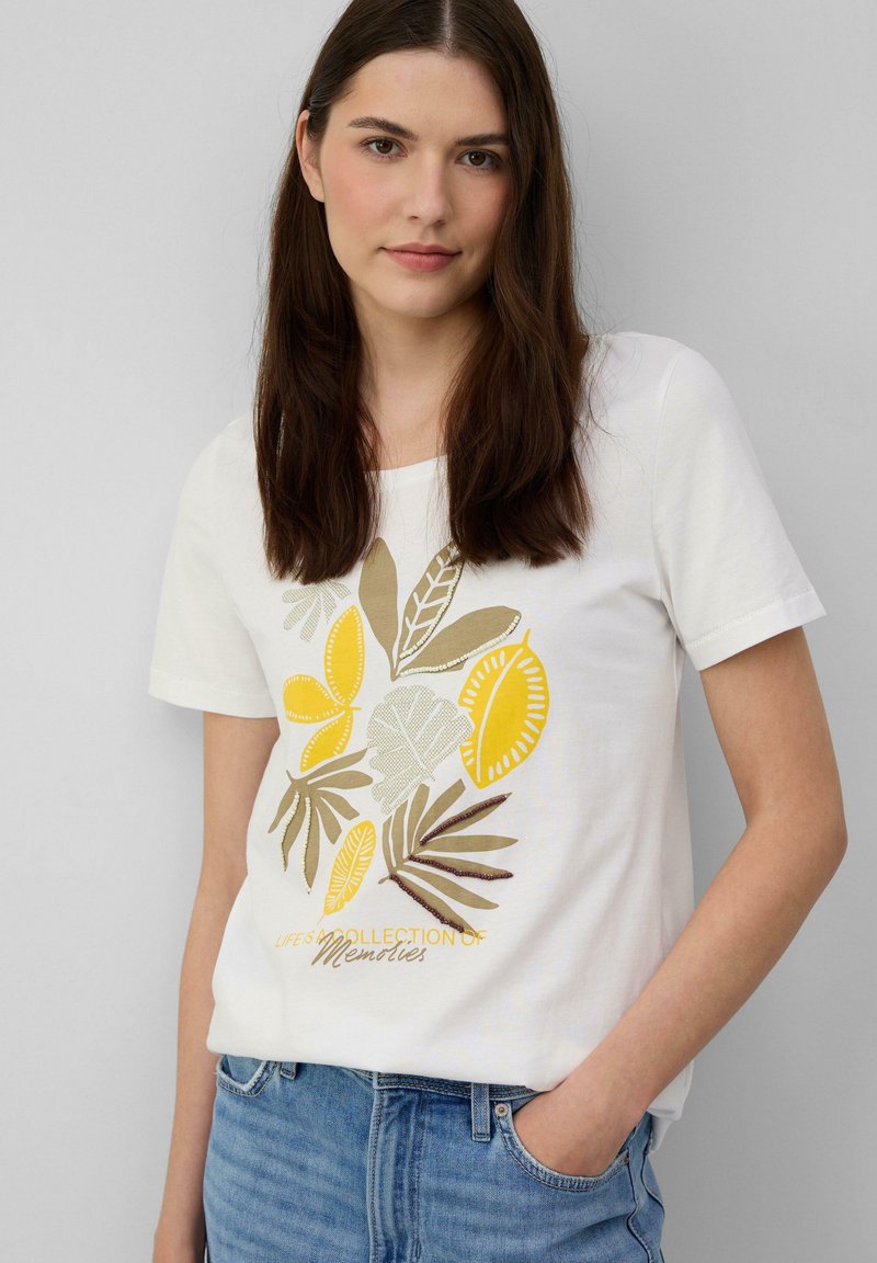 T-shirt en coton blanc avec un imprimé botanique dans des teintes jaunes et vertes, portant la phrase "LA VIE EST UNE COLLECTION DE SOUVENIRS" en écriture cursive.