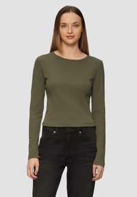 Olivgrünes, langärmliges, eng anliegendes Oberteil mit rundem Ausschnitt, aus geripptem Stoff. Kombiniert mit schwarzen Jeans. Einfaches Design, keine Muster oder Akzente.