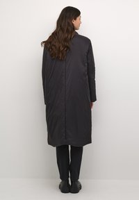 Cappotto lungo, grigio scuro, imbottito con una silhouette dritta e una trapuntatura minimale, dotato di un colletto alto e maniche lunghe.
