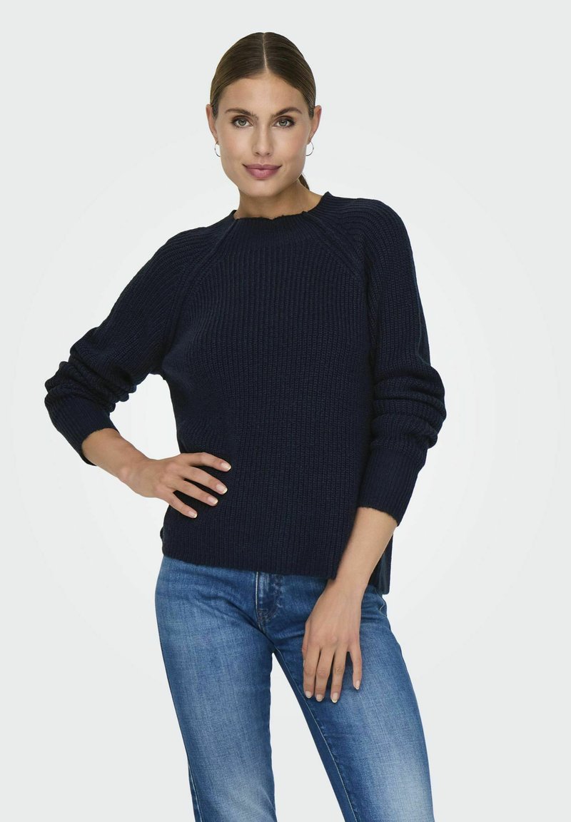 Marineblauer strukturierter Strickpullover mit Raglanärmel, einem runden Ausschnitt und seitlichen Schlitzen, kombiniert mit blauen Jeans.