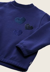 Felpa blu navy con scollo a girocollo. Presenta tre cuori di paillettes in tonalità scure e chiare di blu. Maniche e orlo a cuffia.