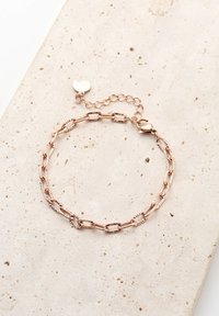 Pulsera de oro rosa hecha de cadenas ovaladas y redondas entrelazadas, con un charm en forma de corazón y una cadena ajustable en longitud con un broche.