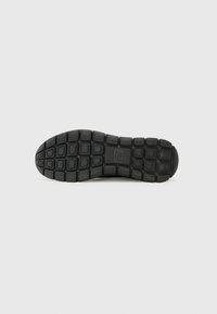 Black rubber shoe sole with textured pattern and rectangular grooves, providing grip and flexibility. The design is functional and durable.