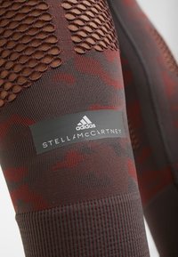 Adidas by Stella McCartney leggings in burgundy and black camo print, featuring mesh panels, ribbed texture, and logo label on waistband.