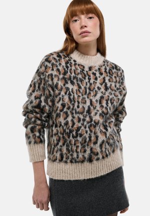 Femme aux cheveux roux portant un pull douillet à imprimé léopard avec des poignets et un ourlet beiges, associé à une jupe gris foncé, sur fond blanc.