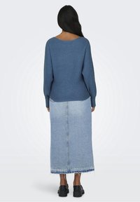 Blå ribbad stickad tröja i kombination med en ljus denim maxikjol med fransad nederkant och svarta platåskor. Bakvy.