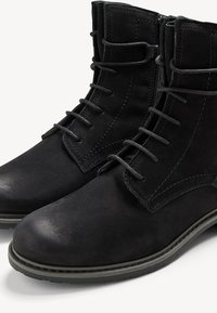 Botines de ante negros con cordones y cremalleras en los laterales. Cuentan con una puntera redondeada y una suela texturizada. Detalle de costura a lo largo de los bordes.