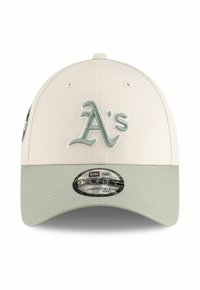 Gorra de béisbol color beige claro con visera verde claro, que presenta un logo bordado de "A's" en la parte frontal y una correa ajustable en la parte posterior.