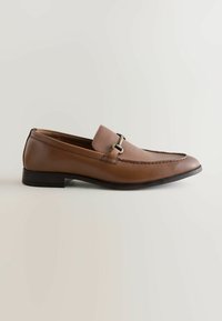 Mocassin pour homme en cuir marron avec empeigne en tissu et détail boucle en métal, semelle plate et petit talon sur un fond clair uni.