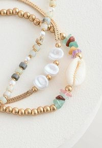 Set di bracciali con perline che presenta perline in metallo color oro, perle di forma irregolare e pietre di vetro colorate, con un accento a forma di conchiglia.