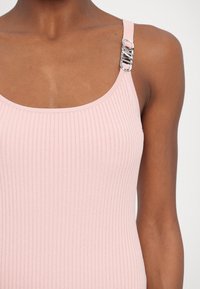 Gros plan sur une personne portant un débardeur côtelé rose pâle avec une boucle argentée sur la bretelle droite.