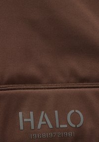 Brunt stof med en glat tekstur prydes af ordet "HALO" i store grå bogstaver, ledsaget af tallene "196819721981" nedenfor.