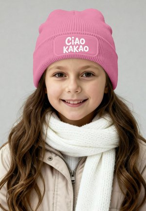 Pink knit beanie with a patch reading "Ciao Kakao," worn with a white textured scarf and a beige zip-up jacket.