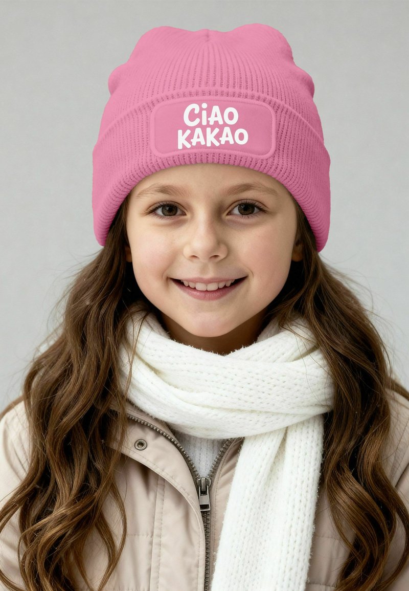 Pink knit beanie with a patch reading "Ciao Kakao," worn with a white textured scarf and a beige zip-up jacket.