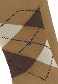 Calza argyle marrone con motivi a rombi beige e marrone scuro e un piccolo logo rotondo nero vicino al centro.