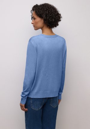 Maglione azzurro chiaro con scollatura rotonda e maniche lunghe, caratterizzato da polsini e orlo a coste. Abbinato a jeans in denim dal taglio ampio.