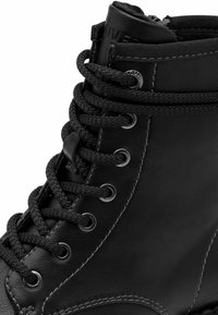 Botte en cuir noir avec une tige haute, bout rond, œillets en métal et lacets tressés. Présente des coutures contrastantes le long du côté et autour du col.
