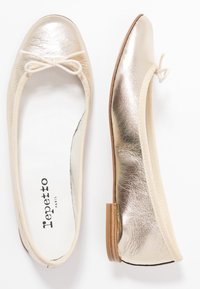 Bailarinas de cuero dorado con punta redondeada y un delicado lazo en la parte frontal. Con un suave ribete elástico y una suela plana de color marrón claro.