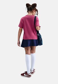 Camiseta rosa de manga corta y falda skater azul marino, combinada con medias altas blancas y zapatillas rojas de Nike, con un bolso azul al hombro.