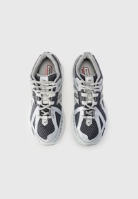 Baskets de sport grises et noires avec une tige en maille, des accents réfléchissants et des lacets blancs. Présente un motif de semelle distinctif pour une meilleure traction.