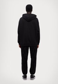 Sudadera negra de corte relajado, combinada con pantalones de chándal negros con un sutil patrón texturizado. Zapatillas completan el conjunto.