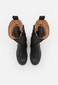Bottes en cuir noir avec une doublure en fourrure marron douce. Elles sont dotées d'une fermeture à glissière et d bords texturés. Le design est haut avec une forme de orteil arrondie.