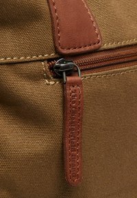 Borsa in tela marrone con accenti in pelle marrone, dotata di cerniera e un tirante in pelle, con texture visibile e cuciture in evidenza.