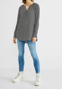 Černobílá vzorovaná košile s dlouhým rukávem a výstřihem do V, ve spojení se světle modrými skinny džíny a bílými vysokými teniskami.