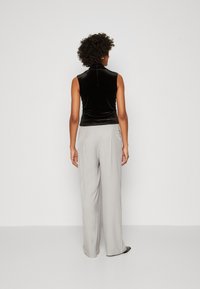 Top sans manches en velours noir associé à un pantalon taille large gris clair. La tenue présente un col montant et des textures subtiles.