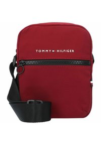 Borsetta a tracolla rossa in nylon con chiusura a zip. Presenta una tracolla nera regolabile e il logo bianco "TOMMY HILFIGER" sul fronte.
