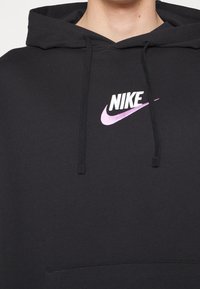 Černá mikina s kapucí z bavlněné směsi, s přední kapsou, kapucí se stahovací šňůrkou a bílým logem Nike s růžovým akcentem. Jednoduchý, neformální design.