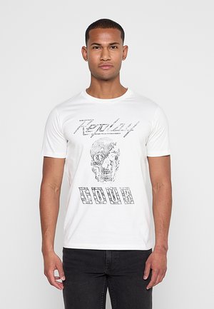 Mann trägt ein weißes T-Shirt mit einer detaillierten Totenkopf-Grafik und den Worten „Replay Hour“ in stilisiertem schwarzem Text.