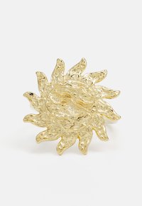 Gul solformet ring med struktureret overflade og bølgede stråler. Designet har et centralt rundt element med udtalte accenter.