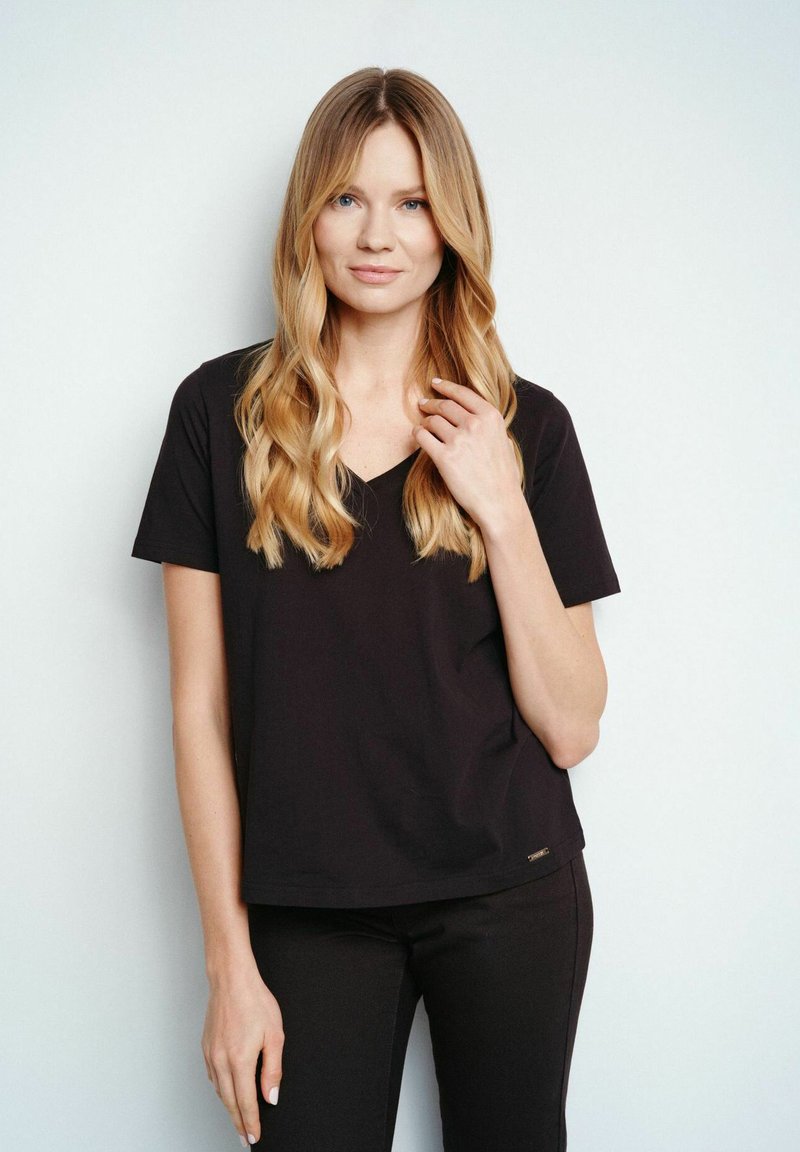 Czarna koszulka polo z dekoltem w serek, wykonana z miękkiego materiału, z krótkimi rękawami i luźnym krojem. Zauważalna metka marki przy dolnym brzegu.