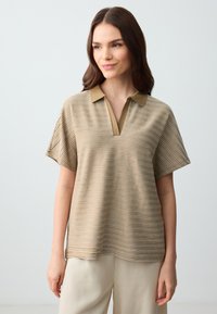 Polo a righe in beige e khaki con scollatura a V, maniche corte e una vestibilità comoda. Tessuto strutturato con righe orizzontali.