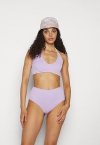 Top de bikini lilás com canelado, decote em V profundo e alças halter, combinado com calções de bikini lilás de cintura alta. Chapéu de balde com padrão de espiral pastel.