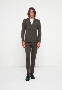 Double-breasted brown suit jacket with notched lapels, two front pockets, paired with matching tailored pants and black shoes.