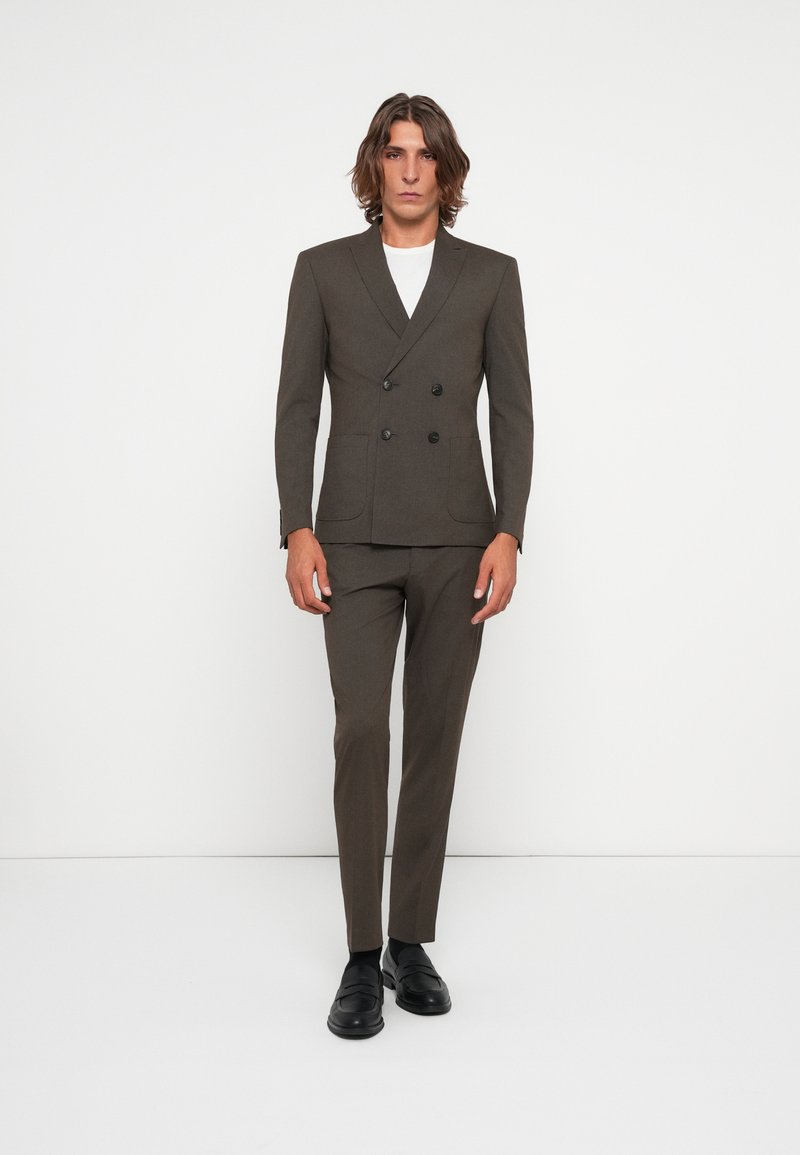 Double-breasted brown suit jacket with notched lapels, two front pockets, paired with matching tailored pants and black shoes.