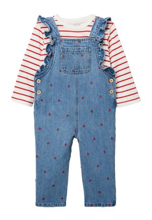 Salopette en denim avec de petits motifs de cœurs rouges et des bretelles volantées, portée sur un chemisier blanc à manches longues avec des rayures horizontales rouges.