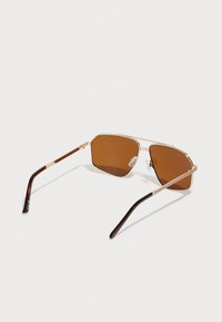 Gafas de sol con tintado marrón, lentes hexagonales, delgado armazón de metal dorado y brazos de carey marrón, con almohadillas de nariz de goma para mayor comodidad.