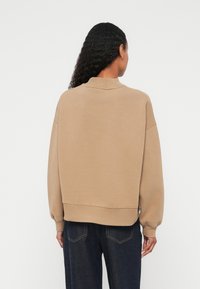 Μπεζ φούτερ με ψηλό γιακά, χαλα ρούς ώμους και ριμπ μανσέτες. Κατασκευασμένο από μαλακό υλικό με άνετη εφαρμογή. Συνδυασμένο με σκουρόχρωμο τζιν.