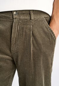 Olijfgroene corduroybroek met verticale geribbelde structuur, voorzakken en een metalen knoopsluiting aan de tailleband.