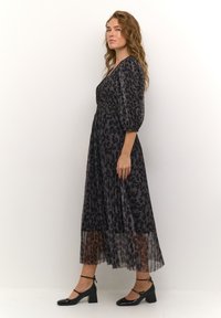 Black leopard print dress with a pleated skirt, v-neckline, and puff sleeves. Pair of black patent ankle-strap heels completes the look.