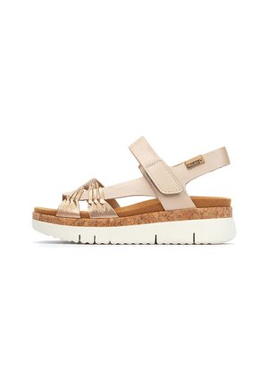 Sandalias beige con suela de corcho, que presentan un diseño de tira texturizada en dorado y cierre de velcro ajustable para un ajuste seguro. Construcción plana y ligera.
